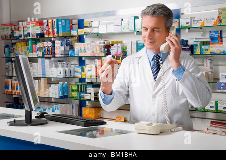Apotheker mit Blick auf eine Droge-Flasche und am Telefon sprechen Stockfoto