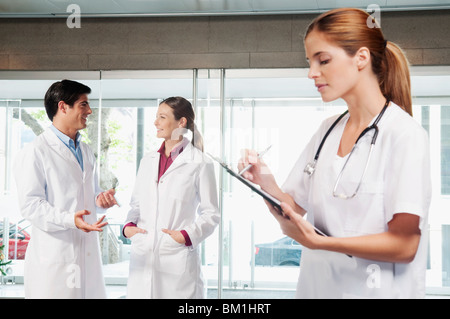 Krankenschwester mit ihren Kollegen diskutieren im Hintergrund auf einem Klemmbrett schreiben Stockfoto