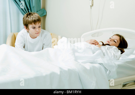 Mädchen in einem Krankenhausbett mit ihrem Bruder sitzt neben ihr Stockfoto