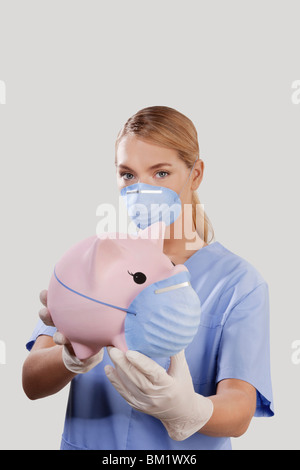 Ärztin, trägt einen Rauchfang-Maske und zeigt ein Sparschwein Stockfoto