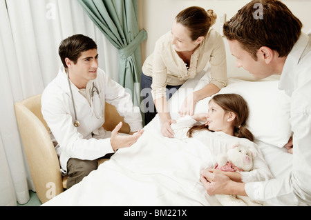 Mädchen auf einem Krankenhausbett und ihre Eltern mit einem Arzt besprechen Stockfoto