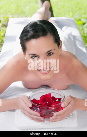 Porträt einer Frau liegend auf einem Massagetisch hält eine Schale mit Rosenblüten Stockfoto