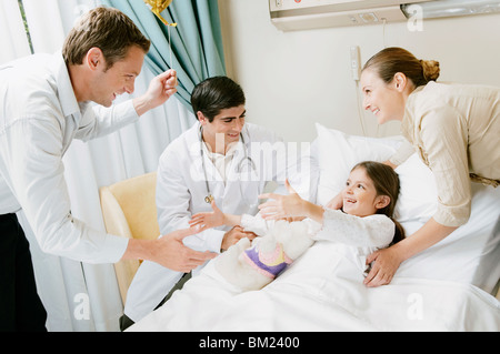 Mädchen auf einem Krankenhausbett und ihre Eltern mit einem Arzt besprechen Stockfoto