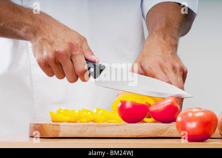Man schneidet eine gelbe Paprika und Tomaten Stockfoto