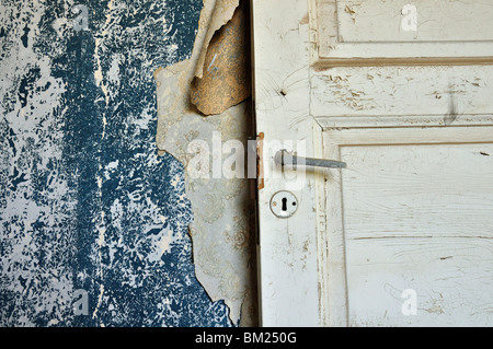 Zerrissene Vintage Tapete blätterte Farbe Wand und Holztür in verlassenen Haus. Stockfoto