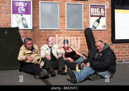 Obdachlose Menschen trinken Alkohol unter Plakate billigen Alkohol in einer Stadt, U.K. Stockfoto