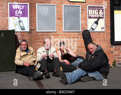Obdachlose Menschen trinken Alkohol unter Plakate billigen Alkohol in einer Stadt, U.K. Stockfoto