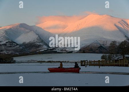 Ein kleines Boot löscht einen Kanal auf einem eiskalten Derwent Water im Winter, Lake District, Cumbria, England, UK. Skiddaw hinter. Stockfoto