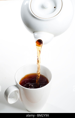 Schwarzer Tee wird aus weißem Tee Topf in weißer Teetasse gegossen Stockfoto
