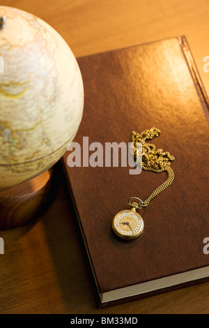 Buch, Globus und Taschenuhr auf einem Schreibtisch Stockfoto