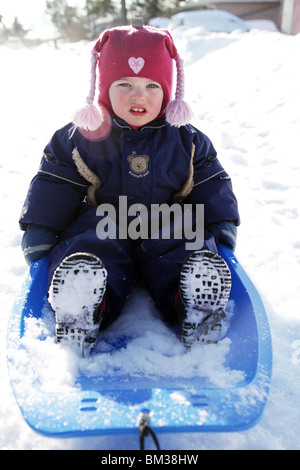 NIEDLICHES KLEINKIND-MÄDCHEN SAT AUF SCHLITTEN IM TIEFEN WINTER: Zwei Jahre altes Mädchen Baby Kleinkind saß sitzend Schneeschlitten-Modell veröffentlicht Stockfoto
