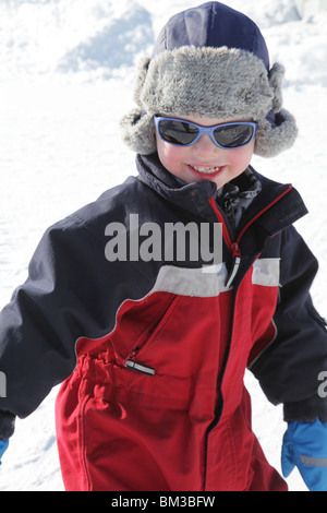 NIEDLICHES KLEINKIND IN SHOW SONNENBRILLE: Ein zweijähriges Baby spielt im Schnee warme Kleidung Sonnenbrille Sonnenbrille Schirme Modell veröffentlicht Stockfoto