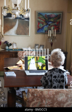 KLEINKIND SCHAUT MOOMINS LAPTOP: Ein zweijähriges Baby, das auf einem Laptop-Computermodell fernsehen für Kinder sieht Stockfoto