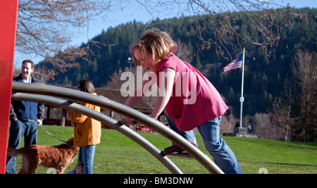 Dieses niedliche kleine Mädchen mit kurzen Haaren ist eine gewölbte Klettern Spielplatzgeräte geprägt. Hintergrund ist absichtlich unscharf. Stockfoto