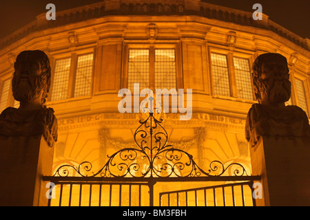 Geschnitzte Steinköpfe, [Sheldonian Theatre] Eingang beleuchtet in der Nacht, Oxford, UK Stockfoto