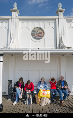 Gruppe von Menschen sitzen auf einer öffentlichen Bank am Pier von Brighton ein gut wissen Besucherattraktion an der Südküste von Sussex Stockfoto