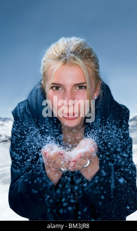 Junge Frau bläst Schnee aus Händen Stockfoto