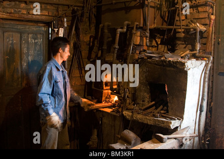 Ein Schmied heizt Metall bis seinen weißen heiß und formbar Kohle befeuerten Ofen in seiner Werkstatt in der Stadt in Sichuan in China. Stockfoto