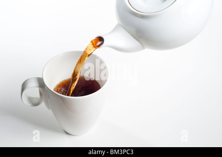 Schwarzer Tee wird aus weißem Tee Topf in weißer Teetasse gegossen Stockfoto