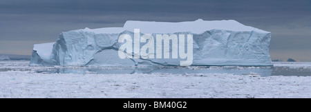 Detaillierte Panoramalandschaften, vorne Licht leuchtenden großen blauen Eisberg floating in gefrorenen eisigen Gewässern der Antarktis unter stürmischen Himmel Hintergrund Stockfoto