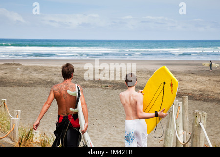 Surfer und Boogie Boarder Piha Strand hinunter wandern. Piha, Waitakere Ranges Regional Park, Auckland, Nordinsel, Neuseeland Stockfoto