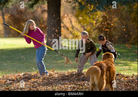 Kinder Rechen und spielen im Herbst Blätter Stockfoto