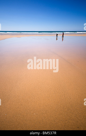 Zwei Menschen, die zu Fuß entlang des Strandes bei Ebbe am Bedruthan Steps in Cornwall, England, UK Stockfoto