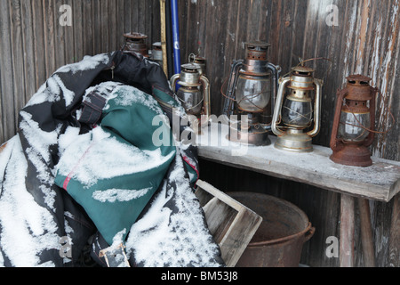 Traditionelle Öl Kerze Laternen stehen außerhalb einer Schnee bedeckten landwirtschaftliches Gebäude mit anderen Geräten in Finnlands Stockfoto
