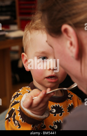 KLEINKIND MIT MAMA, DIE ZEITLÖFFEL FÜTTERT SÜSS: Ein zweijähriges Kleinkind füttert seine Mutter mit einem Teelöffelmodell Stockfoto