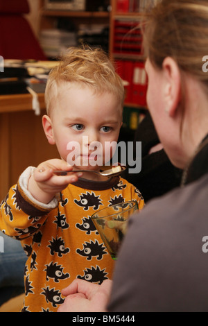 KLEINKIND MIT MAMA, DIE ZEITLÖFFEL FÜTTERT SÜSS: Ein zweijähriges Kleinkind füttert seine Mutter mit einem Teelöffelmodell Stockfoto