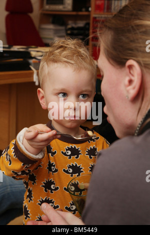 KLEINKIND MIT MAMA, DIE ZEITLÖFFEL FÜTTERT SÜSS: Ein zweijähriges Kleinkind füttert seine Mutter mit einem Teelöffelmodell Stockfoto