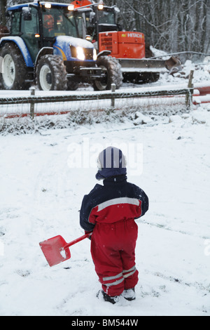 KLEINKIND SPIELT IN FINNLAND TIEFSCHNEE: Ein zweijähriges Kind spielt mit Spielzeugspatschaufel in einem Schneebauwagen-Traktormodell Stockfoto