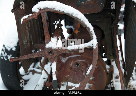 Schnee bedeckt einen Lenkrad auf einen rostigen verlassenen antiken Ford Traktor auf einer Farm in Finnland Stockfoto