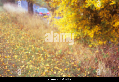 Am frühen Abend Blick vom herbstlichen Bank oberhalb der Straße Autos vorbei mit seiner Rückseite oder Bremsleuchten auf impressionistisch Stockfoto