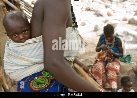 Afrikanische Bedik Frau mit einem Kind dabei Hausarbeit, Iwol Dorf, Bassari-Land, Senegal, Afrika. Stockfoto