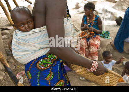 Afrikanische Bedik Frau mit einem Kind dabei Hausarbeit, Iwol Dorf, Bassari-Land, Senegal, Afrika. Stockfoto