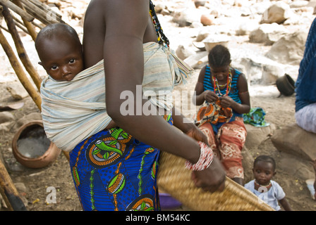 Afrikanische Bedik Frau mit einem Kind dabei Hausarbeit, Iwol Dorf, Bassari-Land, Senegal, Afrika. Stockfoto