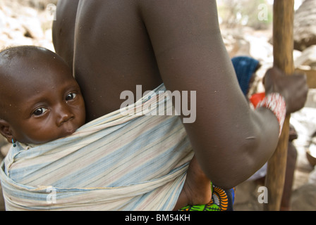 Afrikanische Bedik Frau mit einem Kind dabei Hausarbeit, Iwol Dorf, Bassari-Land, Senegal, Afrika. Stockfoto