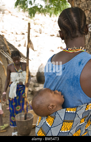 Afrikanische Bedik Frau mit einem Kind während andere Pfund Erdnüsse für Lebensmittel, Iwol Dorf, Bassari-Land, Senegal, Afrika. Stockfoto