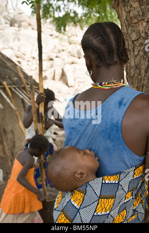 Afrikanische Bedik Frau mit einem Kind während andere Pfund Erdnüsse für Lebensmittel, Iwol Dorf, Bassari-Land, Senegal, Afrika. Stockfoto