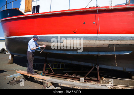 Meister Schiffbauer, John Gaff, Reparatur des Rumpfes eines Fischerbootes mit der traditionellen Methode der Verpackung Bast in Lücken Stockfoto