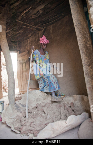 Eine Frau mischt sich kleine Stücke von gebranntem Ton (Grog) mit Tonkörper durch Stanzen drauf in der Töpferei Dorf von Kalabougou in Mali. Stockfoto