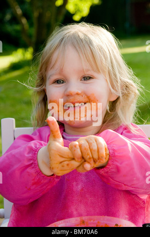 KLEINKIND MÄDCHEN, GENIEßT IMMER CHAOTISCH WÄHREND ESSEN PASTA IN TOMATENSAUCE Stockfoto