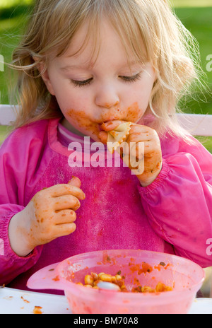 KLEINKIND MÄDCHEN, GENIEßT IMMER CHAOTISCH WÄHREND ESSEN PASTA IN TOMATENSAUCE Stockfoto