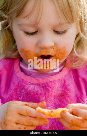 KLEINKIND MÄDCHEN, GENIEßT IMMER CHAOTISCH WÄHREND ESSEN PASTA IN TOMATENSAUCE Stockfoto