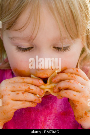 KLEINKIND MÄDCHEN, GENIEßT IMMER CHAOTISCH WÄHREND ESSEN PASTA IN TOMATENSAUCE Stockfoto