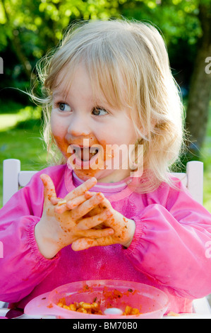 KLEINKIND MÄDCHEN, GENIEßT IMMER CHAOTISCH WÄHREND ESSEN PASTA IN TOMATENSAUCE Stockfoto