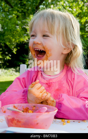 KLEINKIND MÄDCHEN, GENIEßT IMMER CHAOTISCH WÄHREND ESSEN PASTA IN TOMATENSAUCE Stockfoto