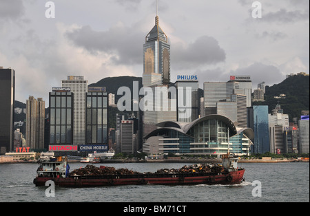 Schrott Metall Lastkahn bewegen west, vorbei an den Wolkenkratzern von Wan Chai Waterfront, Victoria Harbour, Hongkong, China Stockfoto