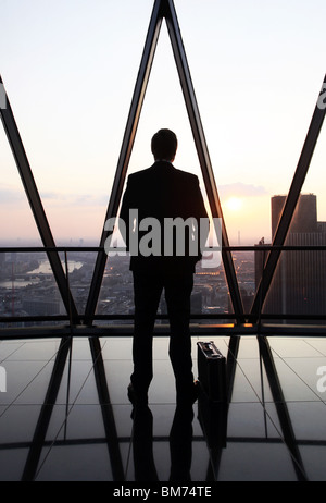 Ein Geschäftsmann Stand mit seiner Aktentasche am oberen Rand der Wolkenkratzer Gherkin in der City of London, U.K Stockfoto